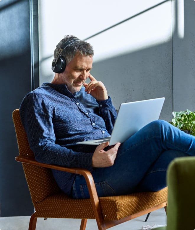 Man with headphones sitting in chair looking at computer happily