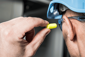A construction worker inserts in-ear ear plugs to fight against hearing loss while working with loud machinery in Florida.