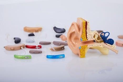 Various styles of hearing aids are displayed next to a model of the inner ear.